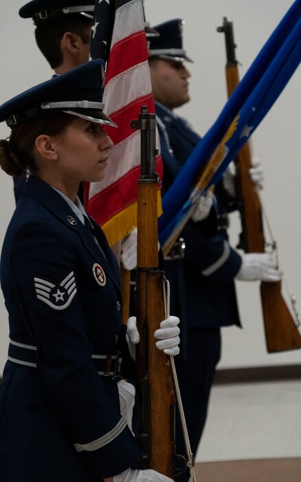 A side profile view of four California Air National Guard honor guard members holding ceremonial rifles and flags during a promotion ceremony.