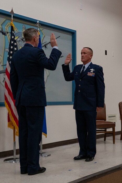 Two California Air National Guard officers raising their hands in front of an Air Force flag as they perform an oath during a premotion ceremony.