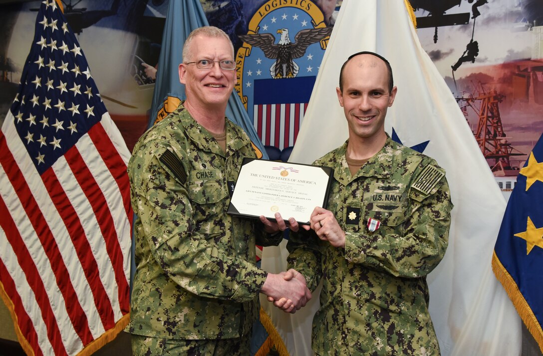 Photo is of two men in US Navy uniforms holding a certificate between them and smiling.