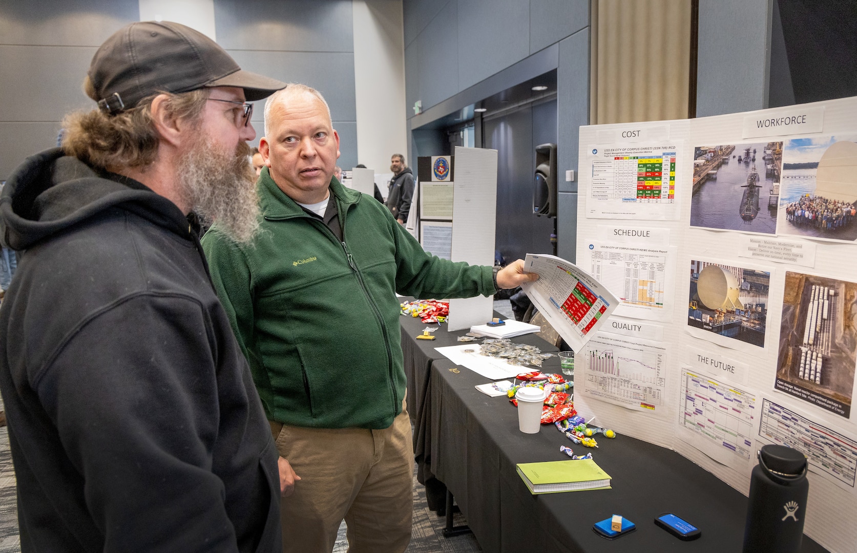 Jack Tappe, project superintendent, Code 350, Inactive Fleet, Reactor Compartment Disposal and Recycling Project, talks about outlines a workforce display for Richard Spencer, shipwright, Shop 64, Shipwrights, Insulators, Plastic Fabric during Code 350’s first-ever Integrated Project Team Development Step III knowledge share fair at the Kitsap Conference Center in downtown Bremerton, Washington, Jan 13, 2023. (U.S Navy photo by Wendy Hallmark)