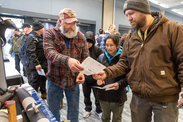 Tracy Steevers, general foreman, Shop 11/17, Shipfitters, Forge, Sheetmetal, stamps passports Jan. 13, 2023, during a Code 350, Inactive Fleet, Submarine Recycling and Reactor Compartment Disposal knowledge fair at the Kitsap Conference Center in downtown Bremerton, Washington. (U.S. Navy photo by Wendy Hallmark)