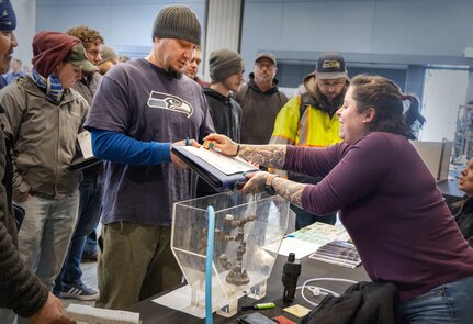 Shellby Norwood, tank coordinator, Code 350, Inactive Fleet, Reactor Compartment Disposal and Recycling Project, stamps visiting employees' passports during their first-ever Integrated Project Team Development Step III knowledge share fair at the Kitsap Conference Center in downtown Bremerton, Washington, Jan 13, 2023. (U.S Navy photo by Wendy Hallmark)