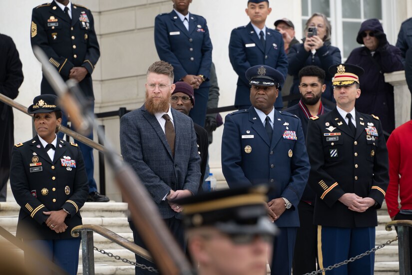 A group of military members standing and watching a ceremony.