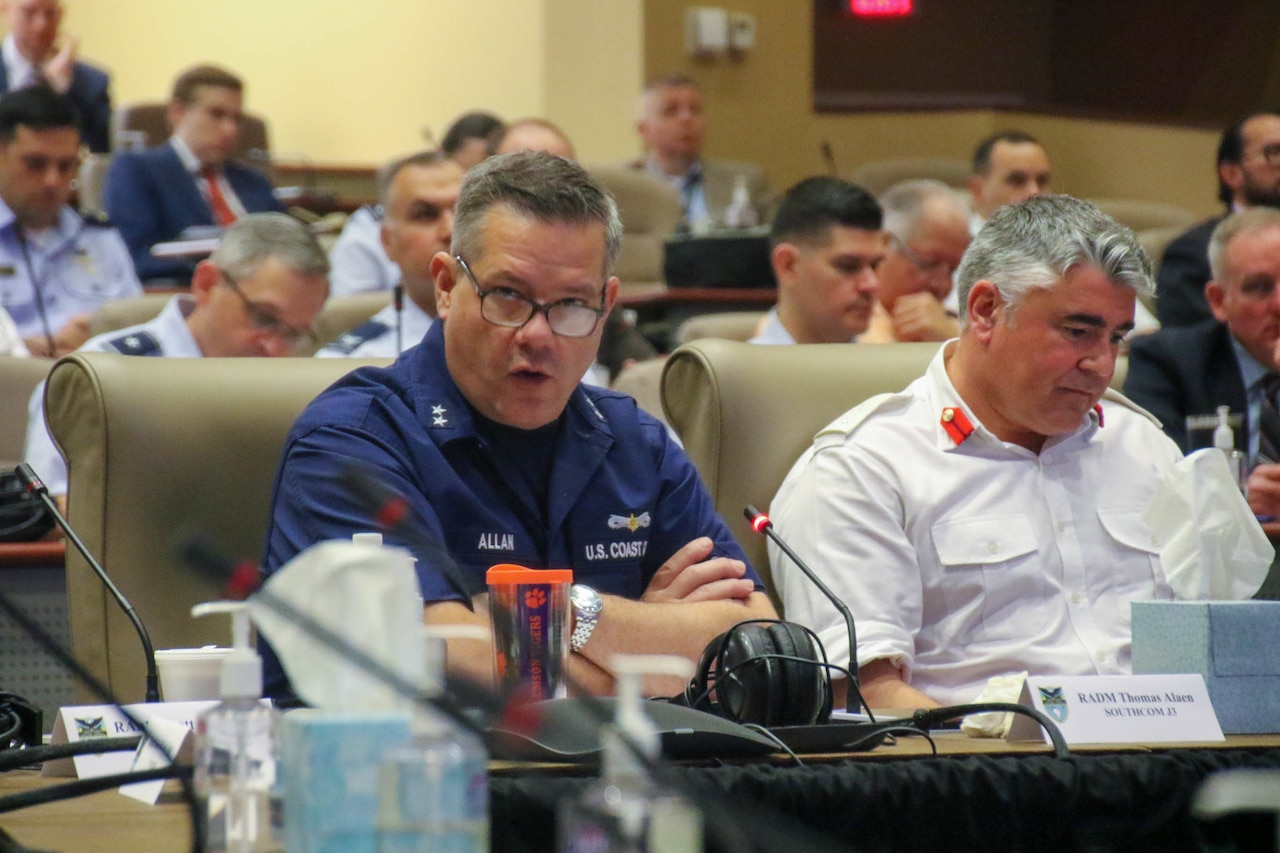 Service members sit at long tables during a conference.