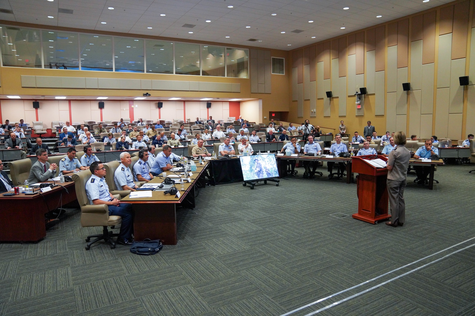A military conference is held in a large room.