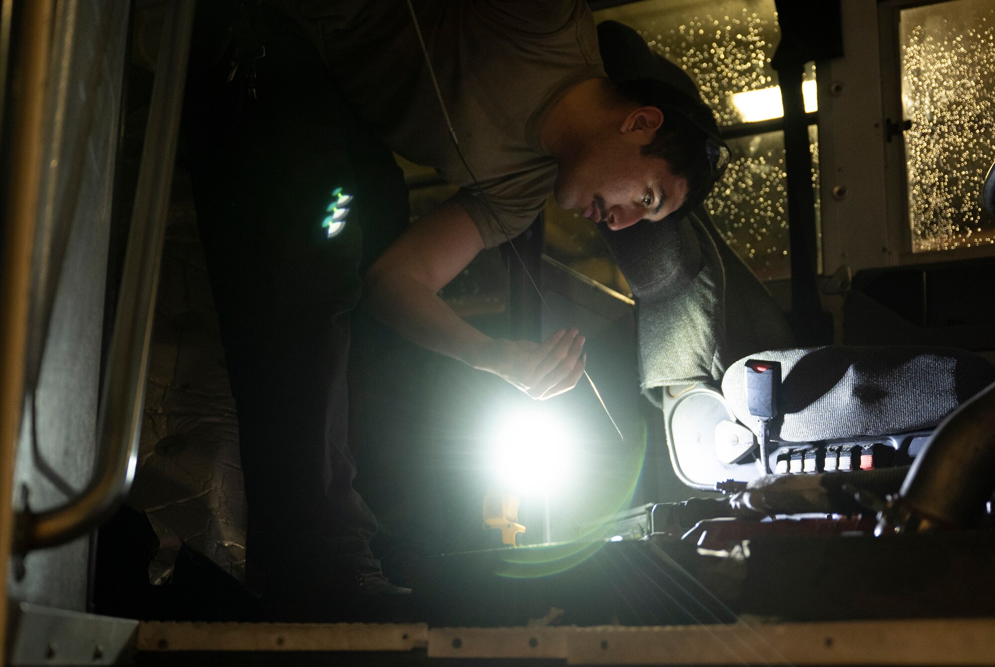 USAFR 307th LRS Senior Airman works on a piece of equipment while using a flashlight to illuminate his workspace.