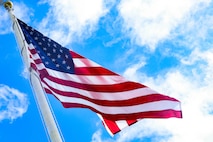 An American flag waves against a blue, cloud-dotted sky.