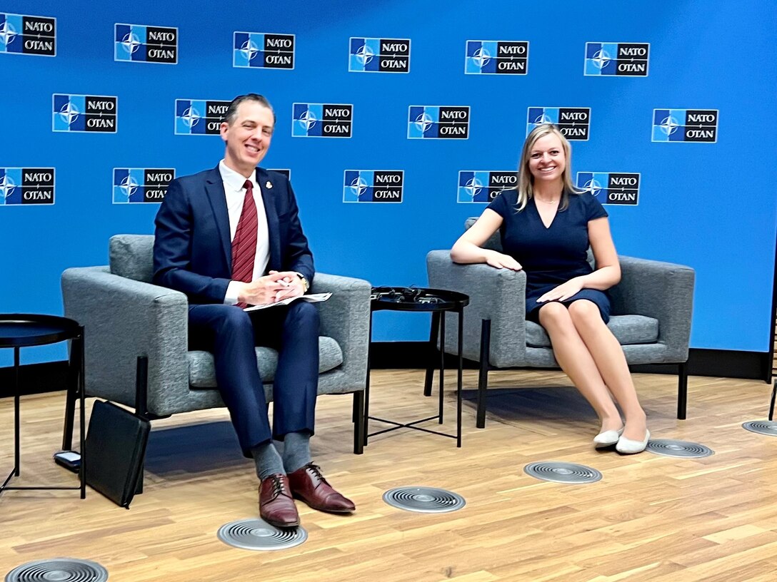 Two researchers siting while posing for photo during a presentation to NATO.