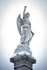 Statue of an angel with a dusting of snow on it. The angel is pointing up to the sky with one hand and holding a sword in the other.