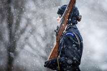 Soldier wearing cold weather uniform carrying a rifle on her sholdier while marching in snowy weather conditions.