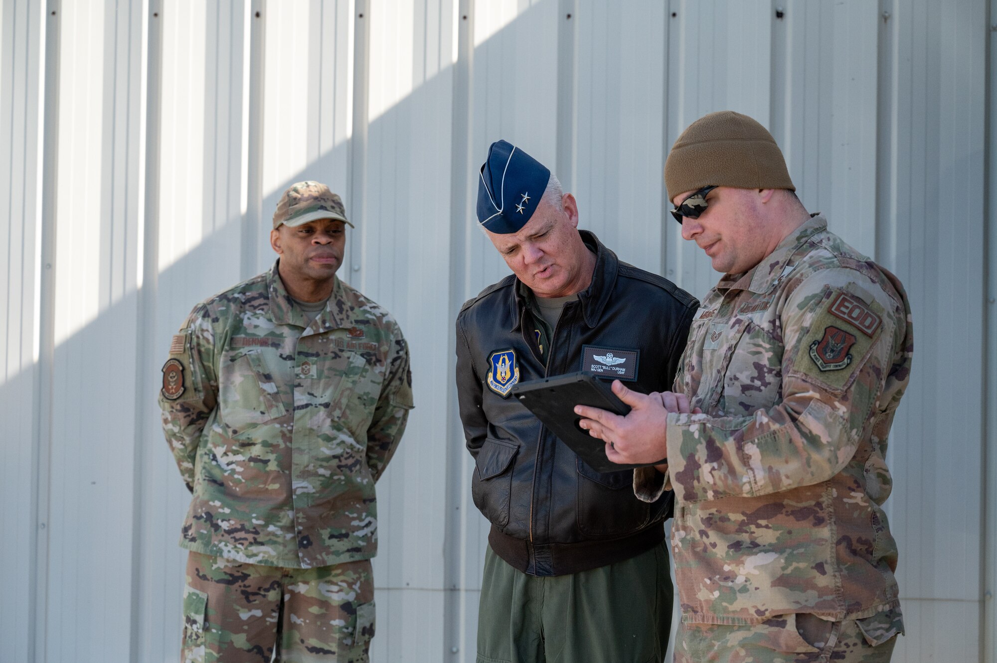 Three men, each in military uniform, are lined in an imperfect, slightly circular row. The one at far right, identified as Chief Master Sgt. Travon Dennis, onlooks as Tech. Sgt. Rogerito Miravetedisantis explains something on an tablet to Maj. Gen. D. Scott Durham, middle.