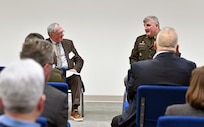 Two men sitting in front of group talking.