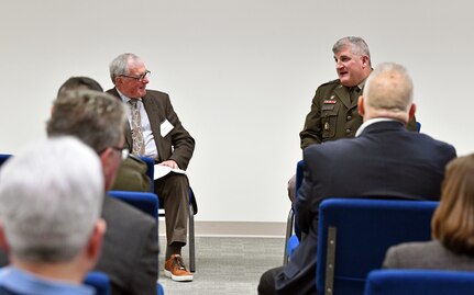 Two men sitting in front of group talking.