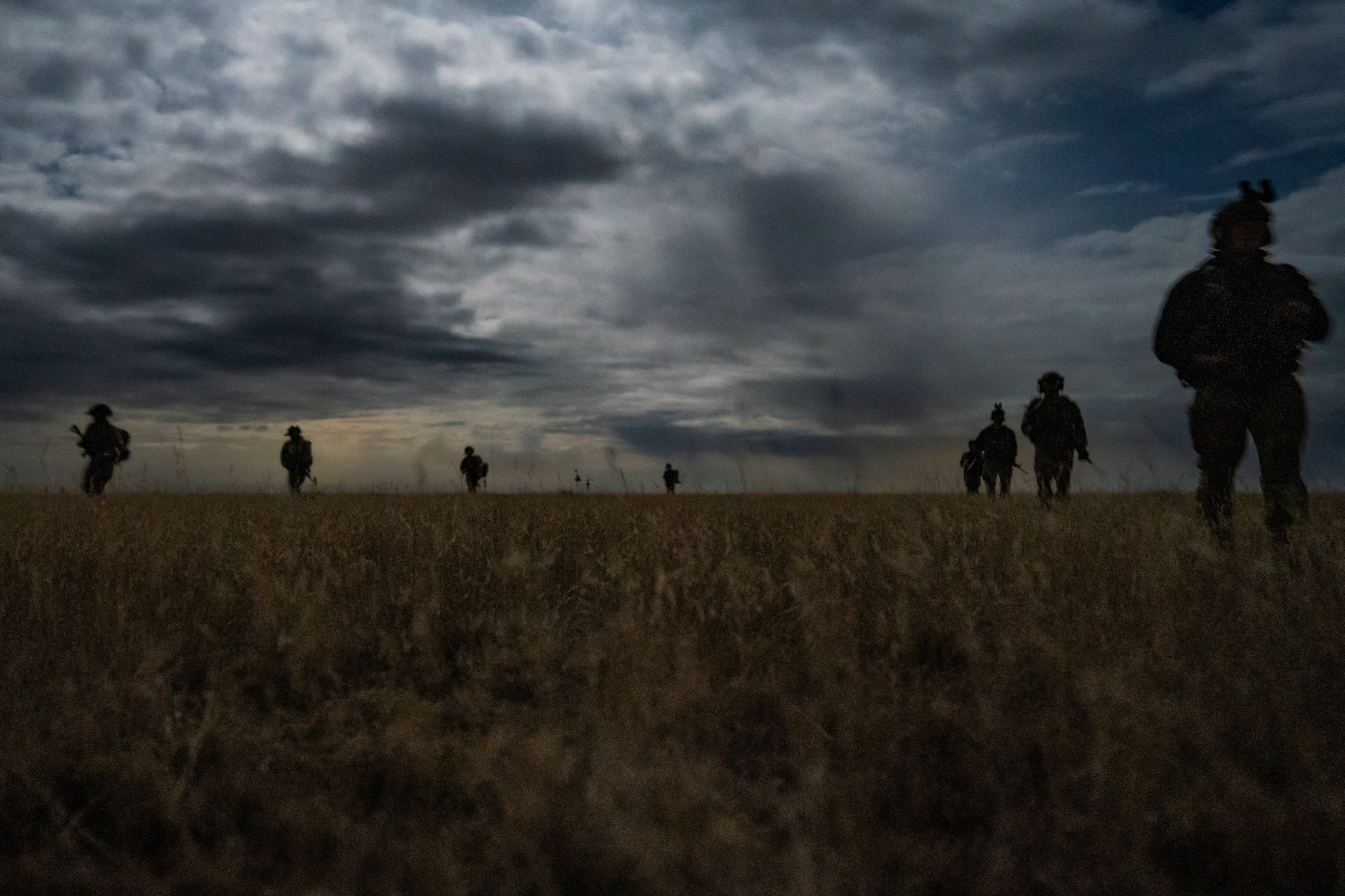 Eight silhouetted men armed with rifles walk in two lines over an open prairie.
