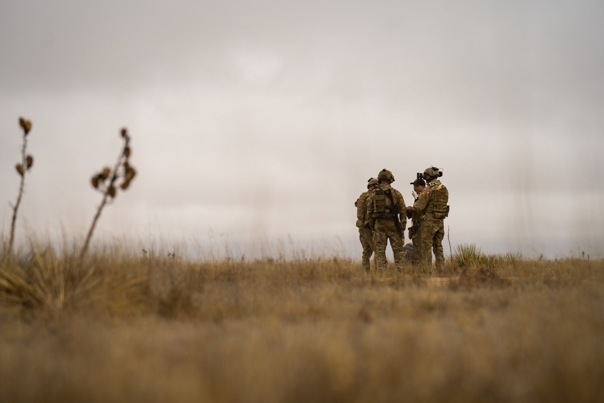 Four men in military uniform stand huddled in the distance of a praire.