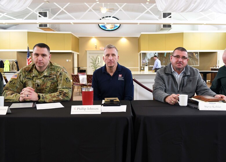 Three middle aged men sit at a table in an event hall.