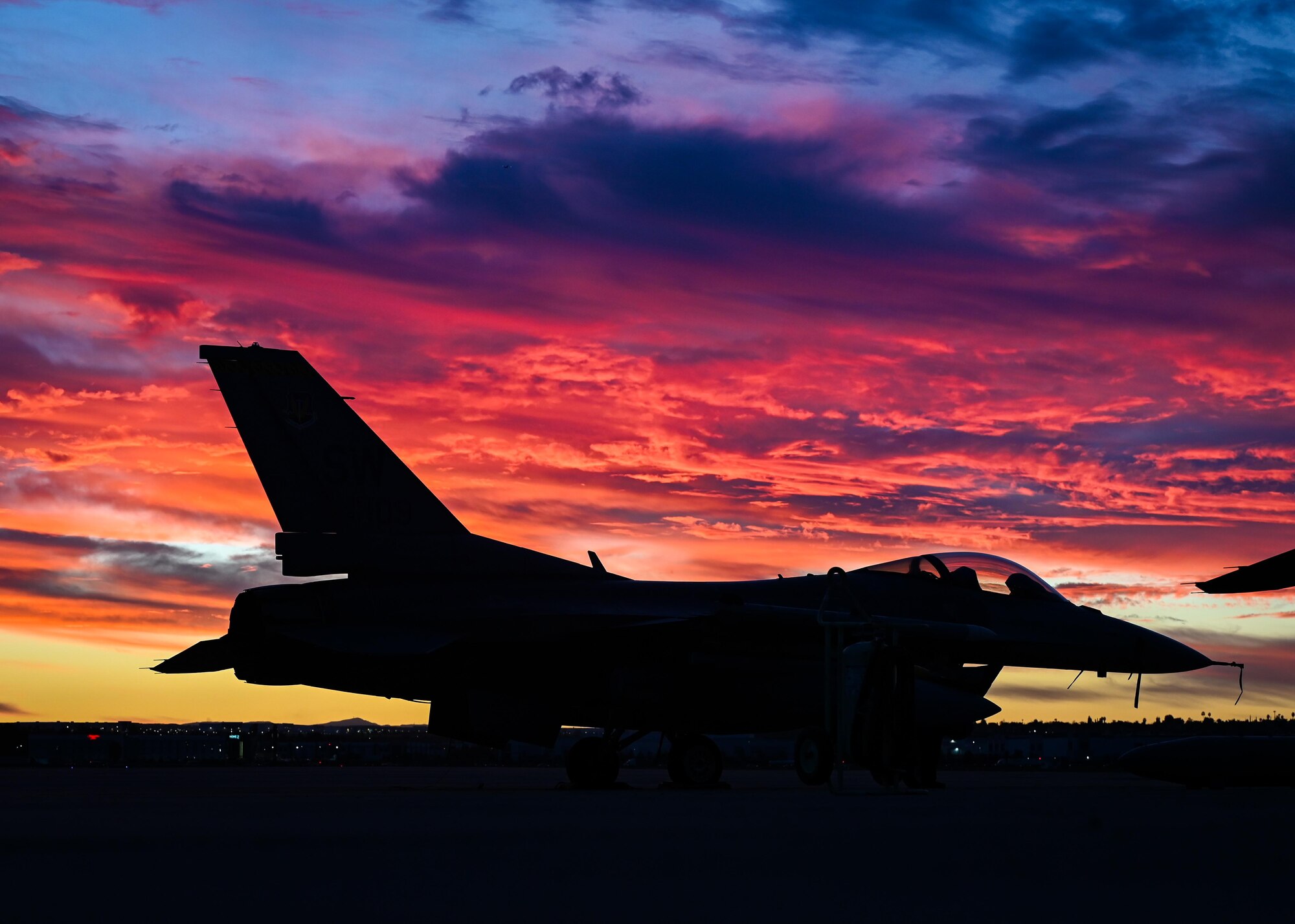 A silhouette of an F-16C Fighting Falcon sitting on the flightline during sunset.