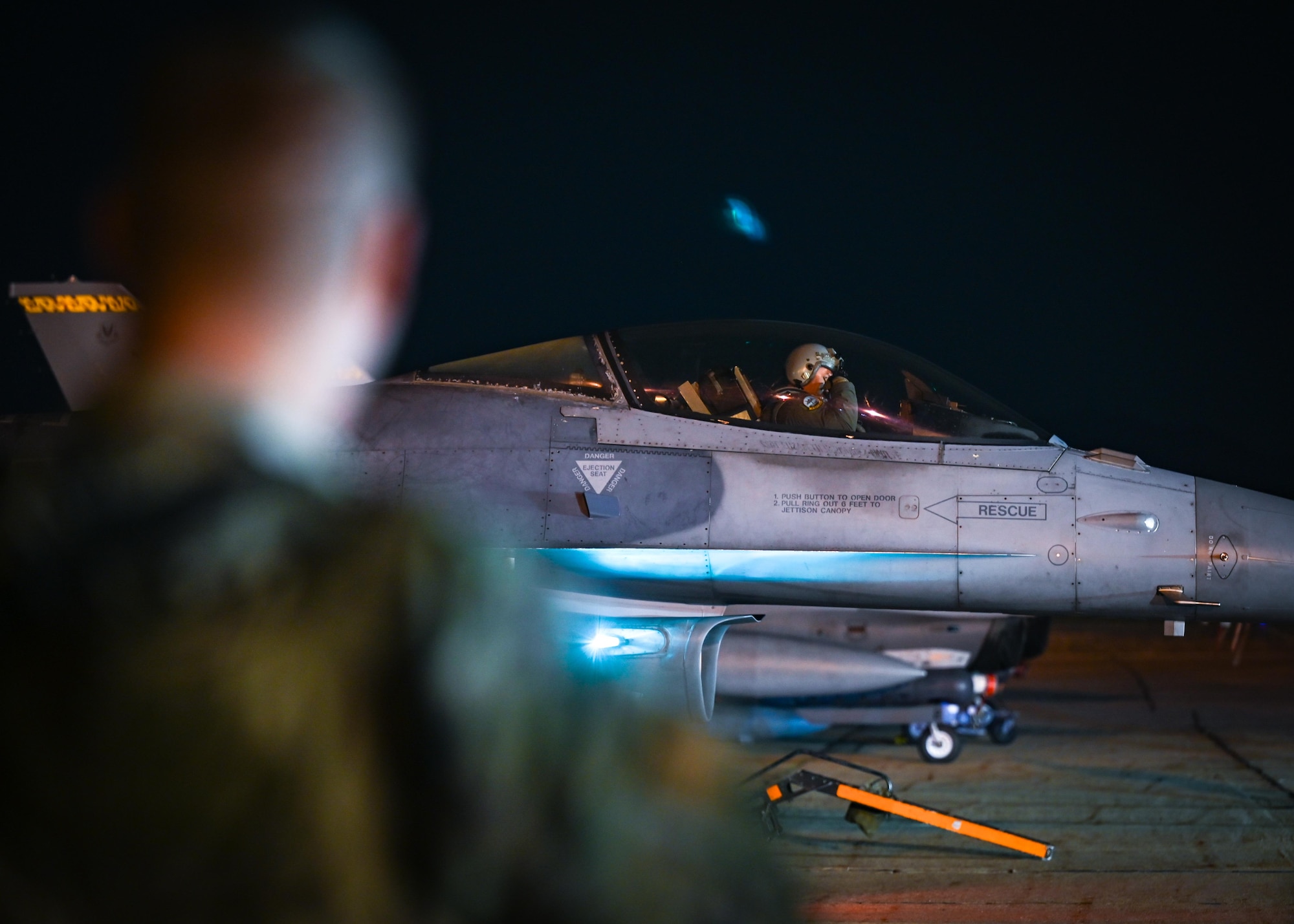 A security forces Airman looks over at an F-16C Fighting Falcon.