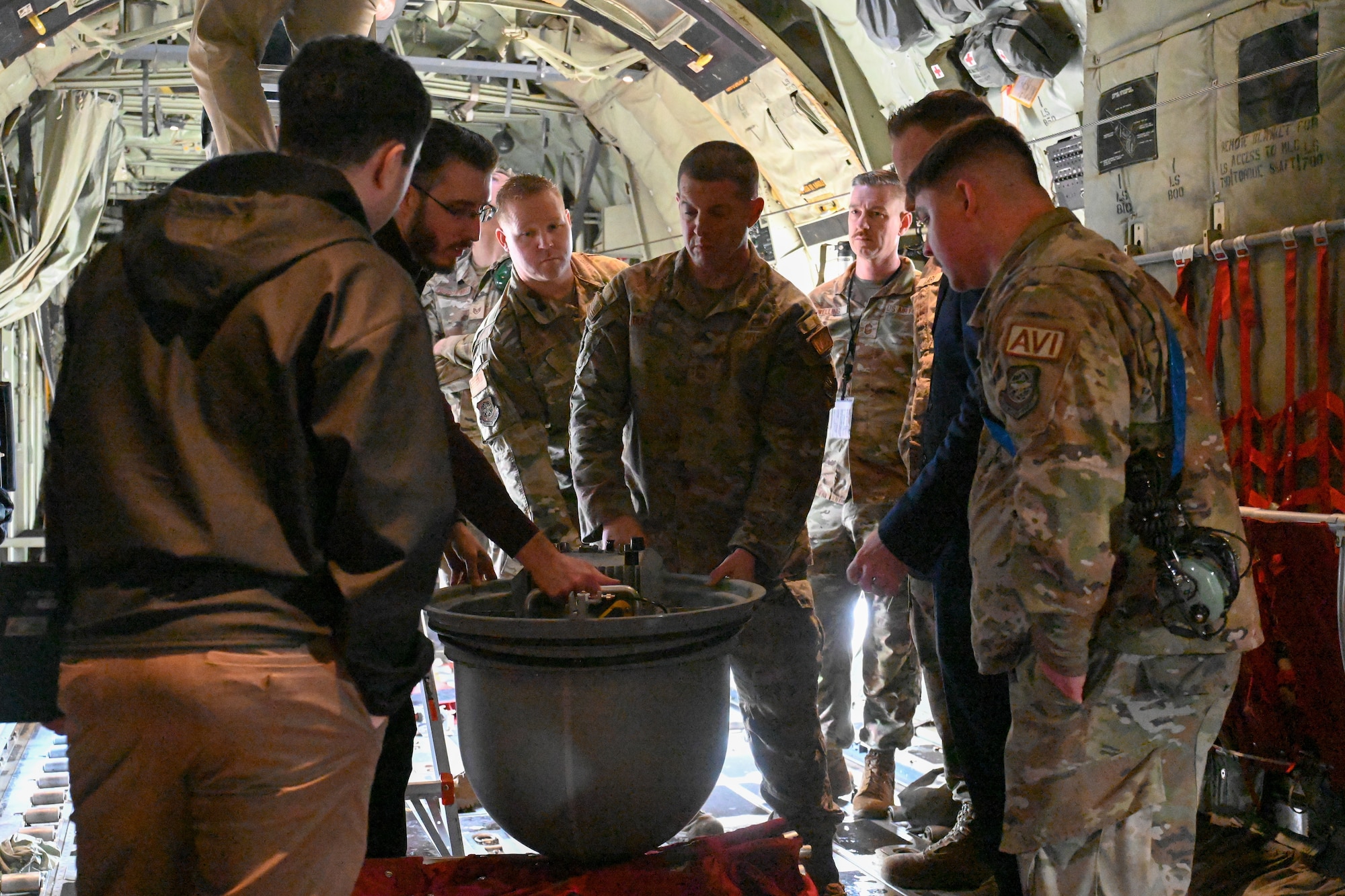 Airmen and contractors stand around a communication pod inside of a C-130J.