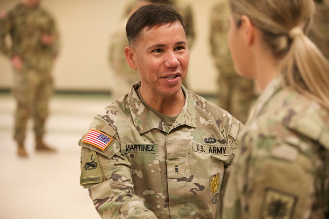 A male uniformed soldier shakes hand with a soldier while smiling.