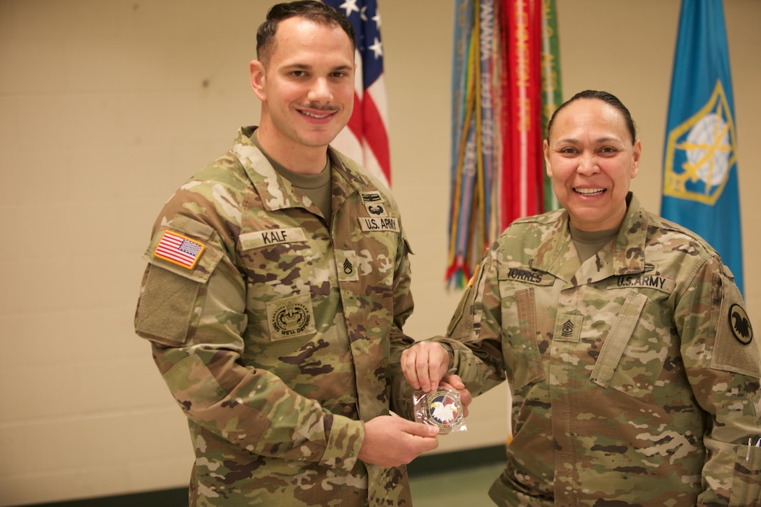 A uniformed soldier presents a coin to another soldier.