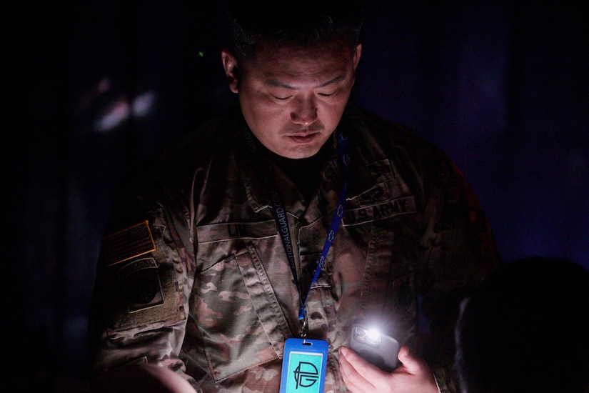 A soldier holds a light while reading something in a dark room.