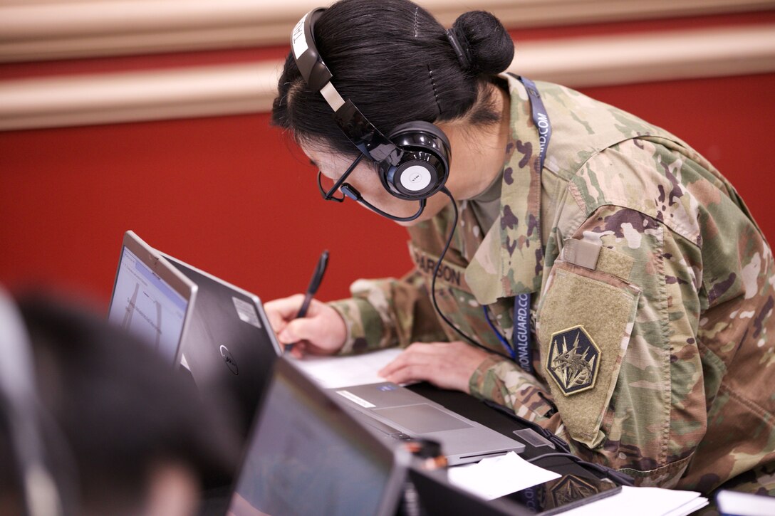 A soldier wearing headphones writes something down.