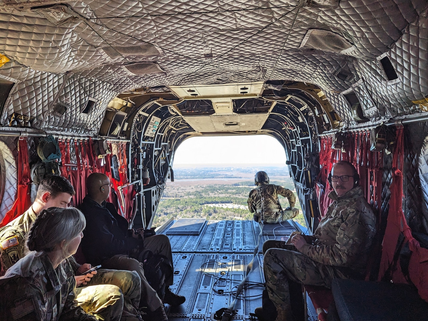 Photo of U.S. Soldiers, U.S. Airmen, and a Department of Defense civilian riding in the back of a Chinook helicopter to observe training activities during the exercise Maple Thunder in Savannah, GA, Jan. 29, 2024.