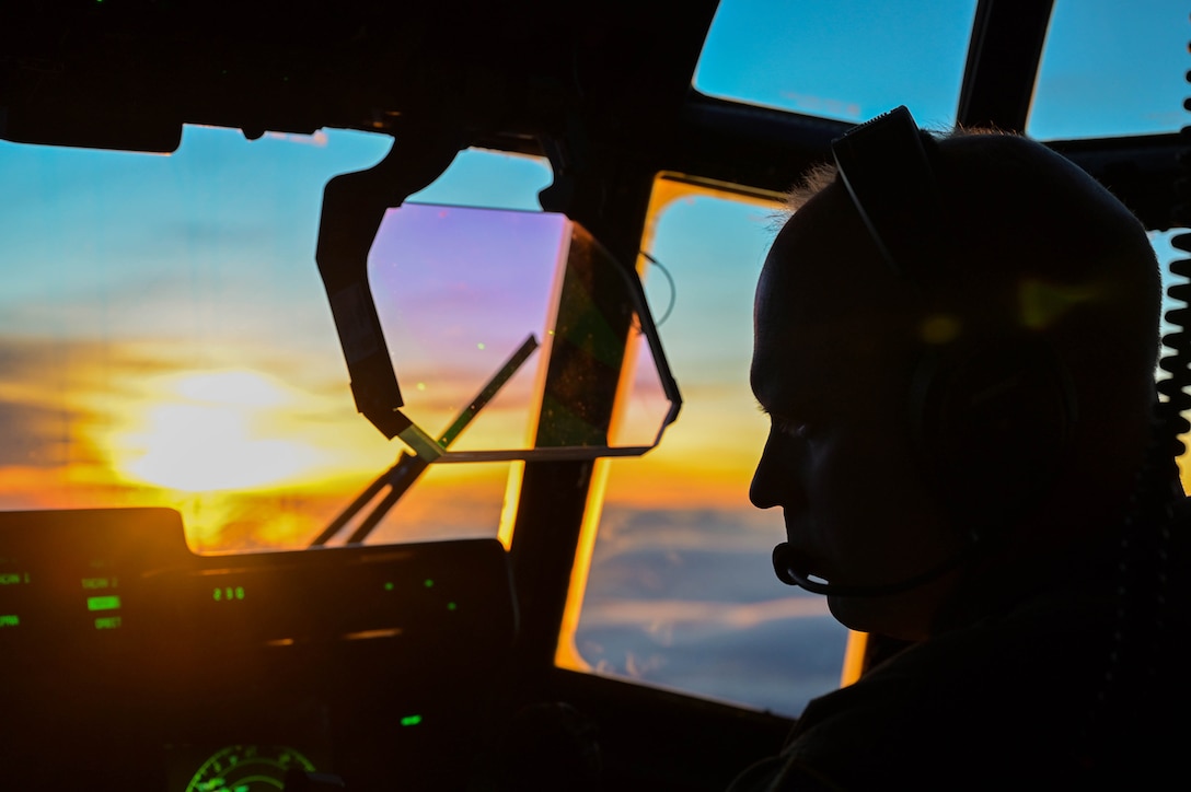 Close-up of an Air Force pilot in silhouette looking down at the control panel in a cockpit with a low-set sun in the background.