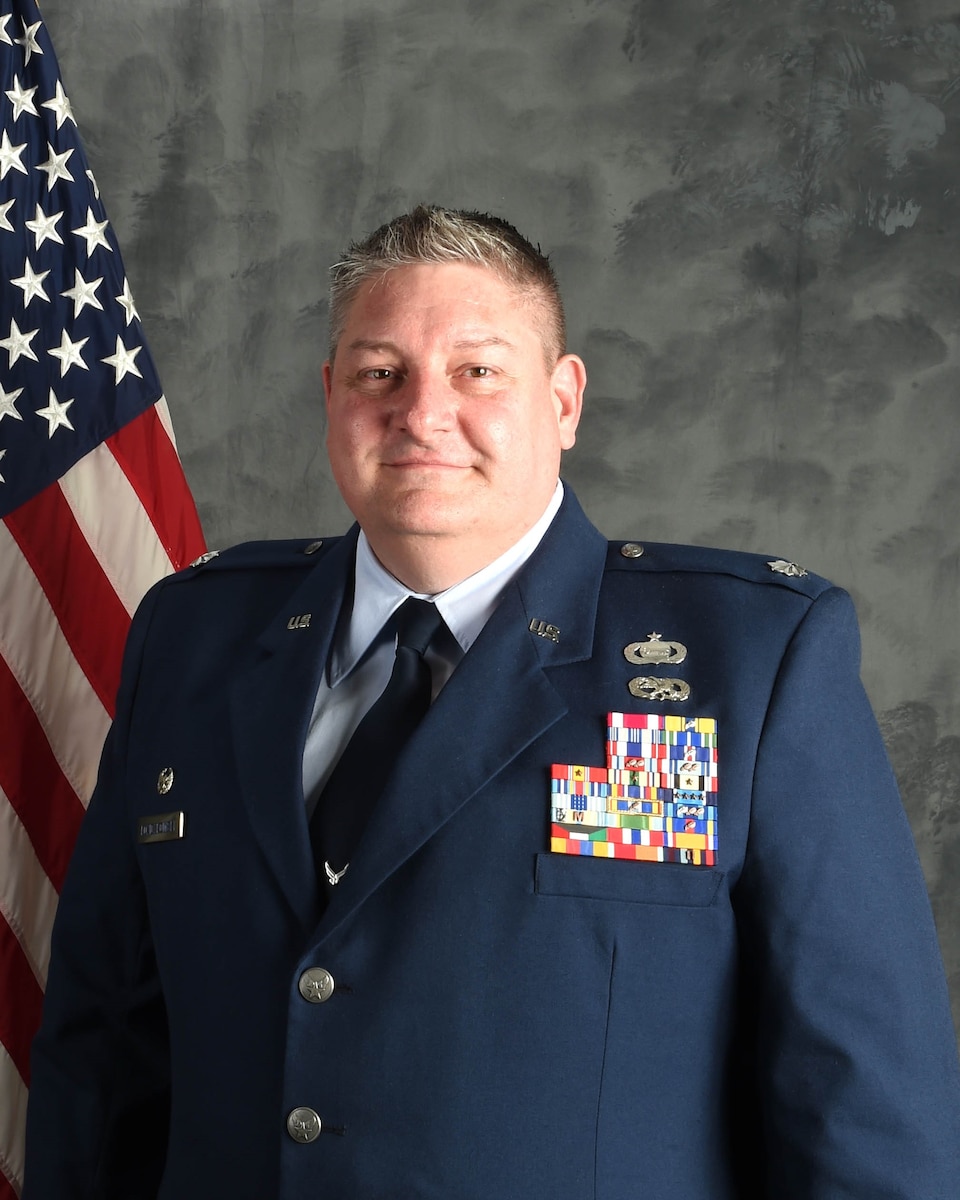 Man in Air Force dress blue uniform poses for photo in front of American flag