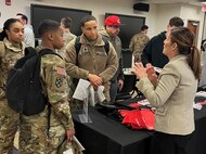 Men and women wearing u.s. army uniforms talk to people standing people from a university.