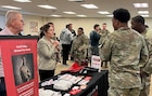 Men and women wearing u.s. army uniforms talk to people standing people from a university.