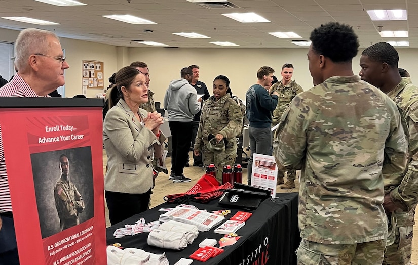 Men and women wearing u.s. army uniforms talk to people standing people from a university.