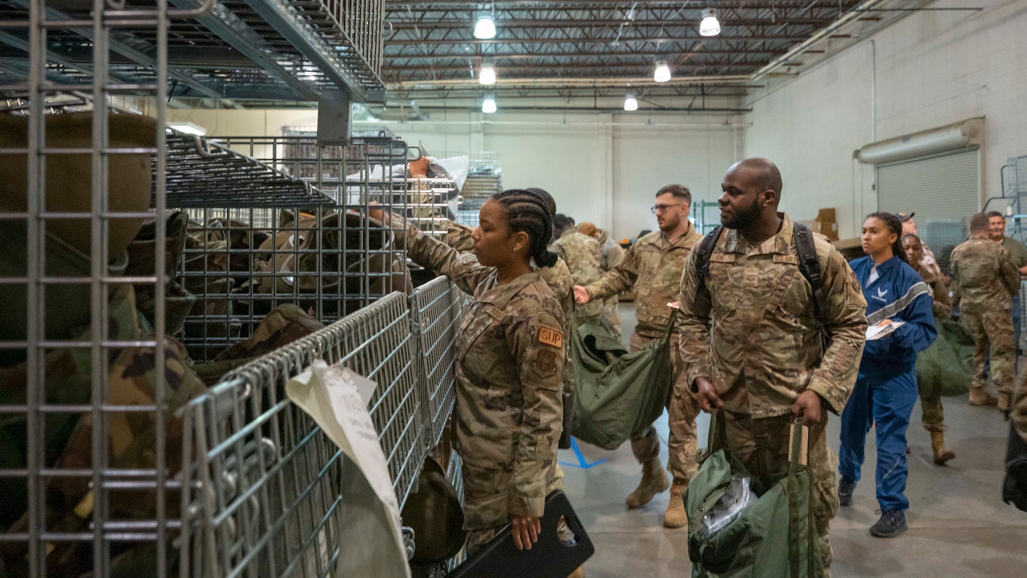 Several airmen in single-file line receive chemical protective equipment in a warehouse.