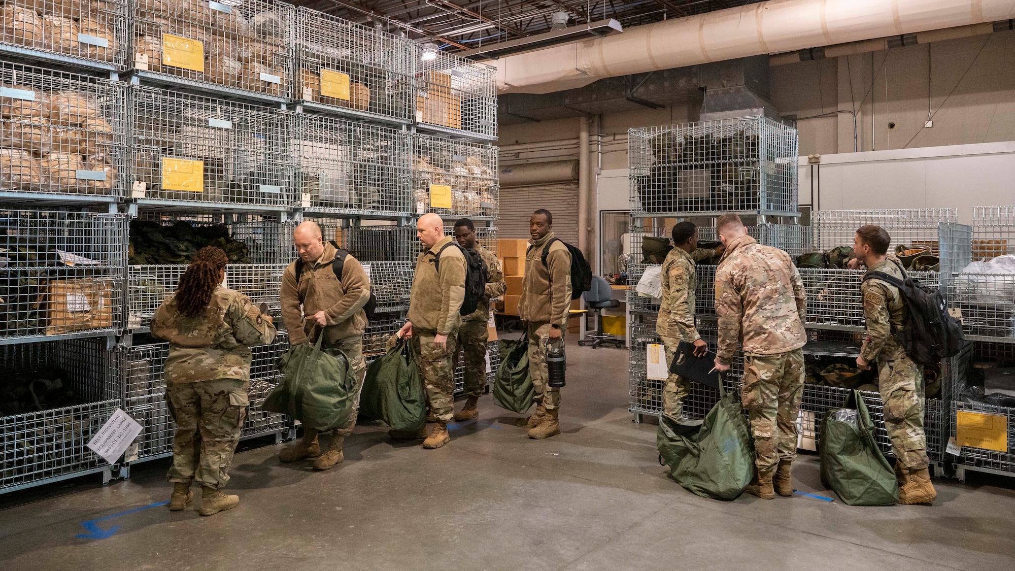 Several airmen in single-file line receive chemical protective equipment in a warehouse.