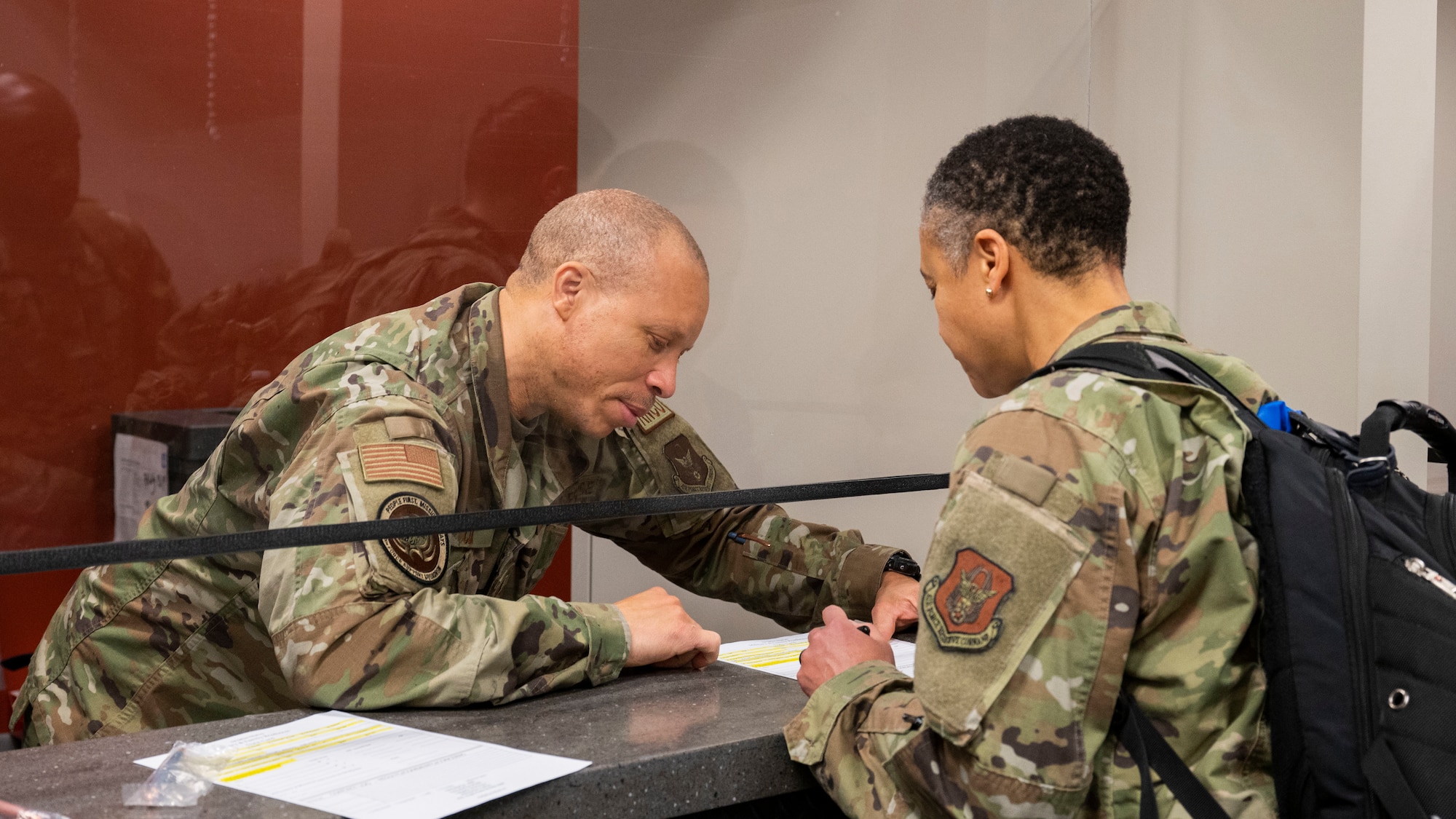 An airman behind a counter reviews deployment paperwork with another airman during a simulated deployment out-processing line.