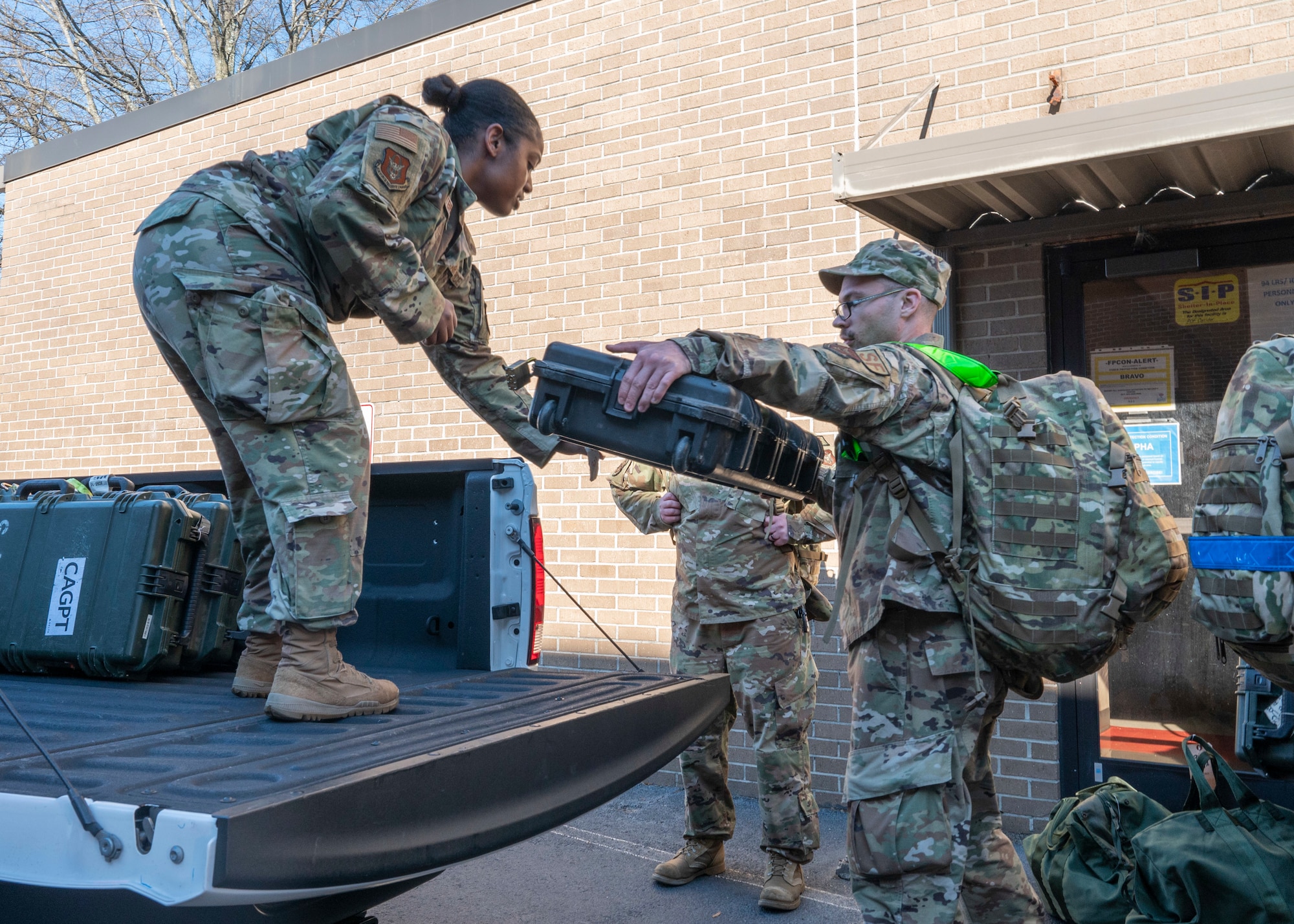 An airman passes a large case to another airman standing on a truck bed, where additional cases sit.