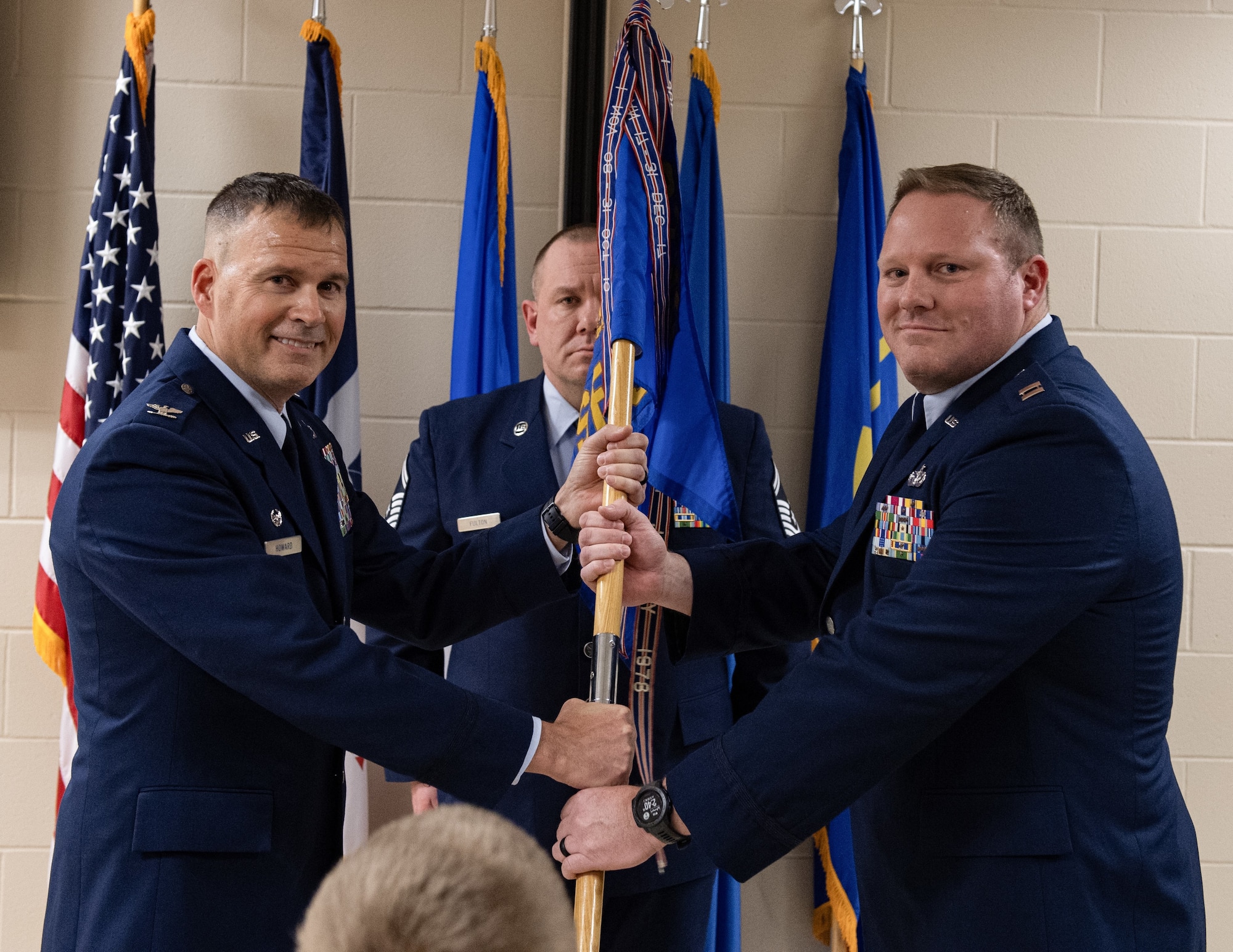 Two Airmen in dress blue uniforms grip a banner while posing for a photo