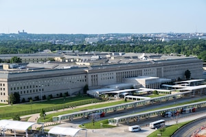 An aerial view of the Pentagon with trees and Washington, D.C. in the distant background.