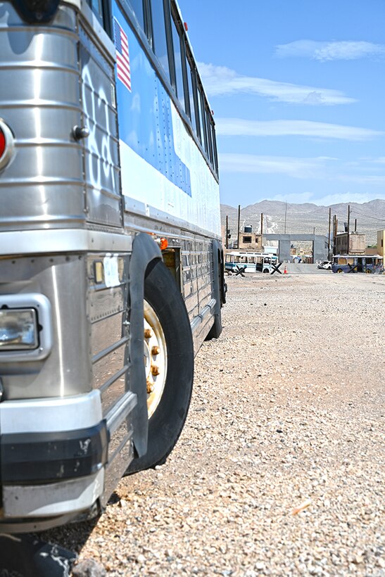 A passenger bus in the foreground, a desert village in the background.