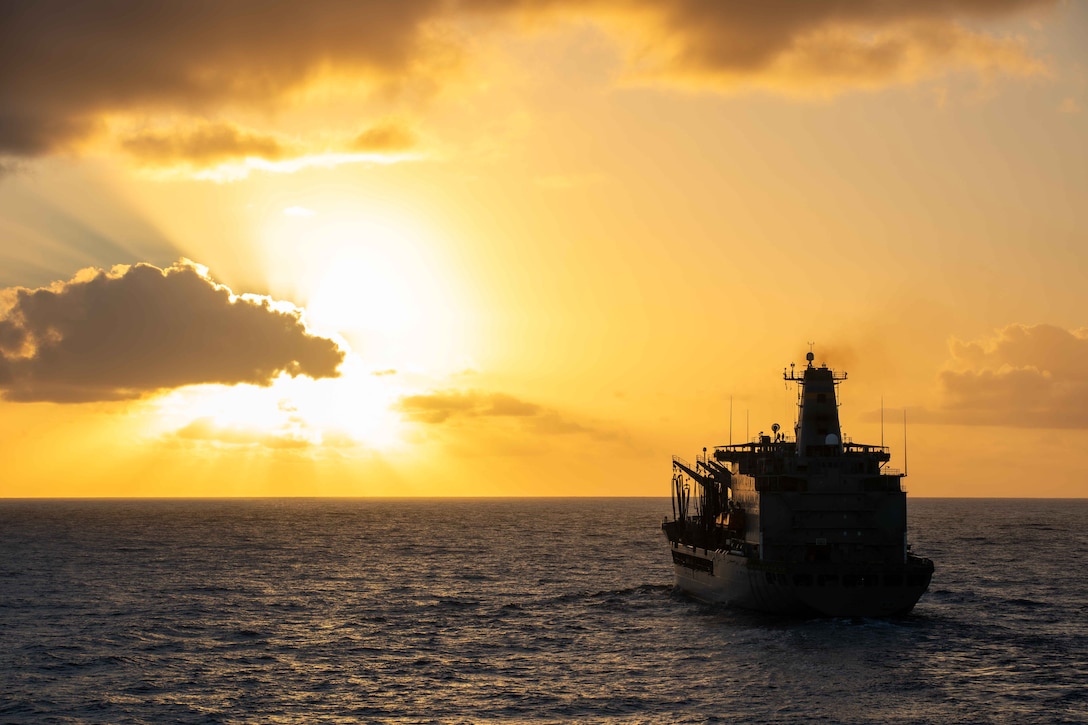 A large ship steams across the water as the sun breaks through the clouds.