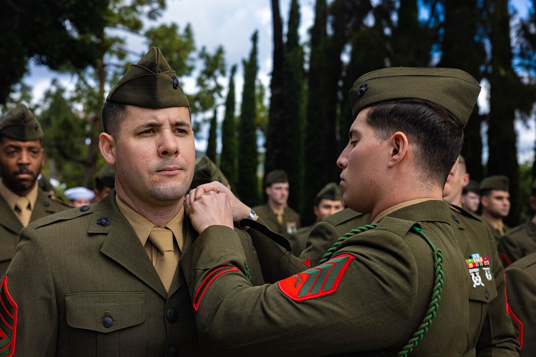 A uniformed service member attaches a French Fourragere rope to another service member’s uniform.