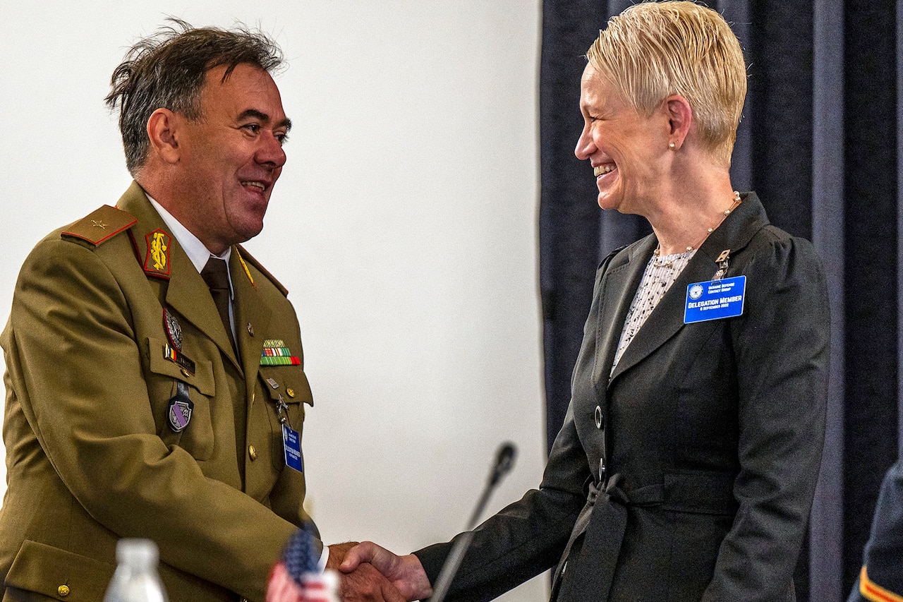 A person in a business suit shakes hand with a person in a military uniform.