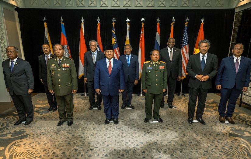 A group of people stand in two rows for a picture. There are flags behind them.