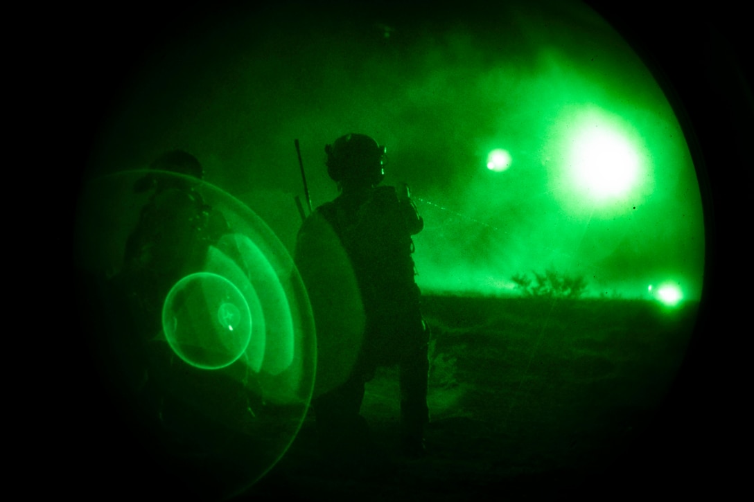 A soldier aims a laser onto the ground below lights from an approaching helicopter as seen through night vision lens.