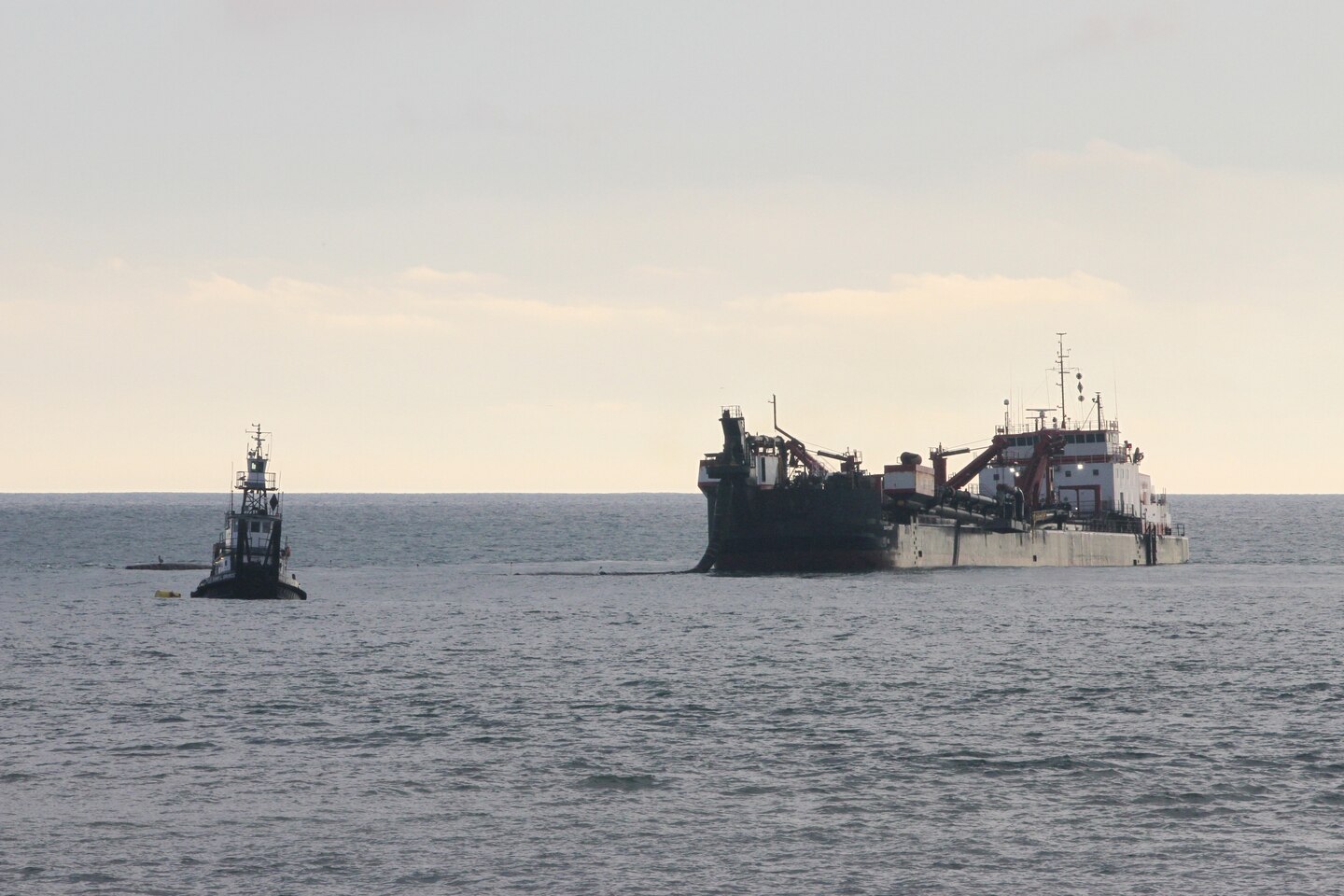 A split-hull trailing suction hopper dredge, linked to a tugboat, operates Jan. 31 off the shore of Solana Beach, California.