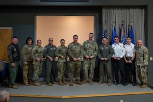 Several men and women stand on a stage, most with awards in their hands. All people visible are wearing a variation of a U.S. Air Force uniform.