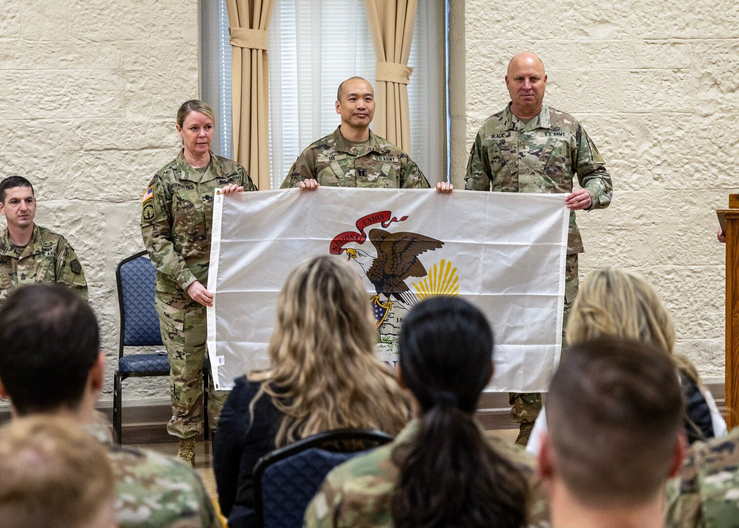 Lt. Col. Beth Roxworthy (left), Commander of the 34th Division Sustainment Brigade, and Chief Warrant Officer 5 Thomas Black (right), State Command Chief Warrant Officer for the Illinois Army National Guard, present Capt. Simon Lee (center), Logistics Advisor Team 6612 Team Leader, with the Illinois flag that will accompany them on their deployment.