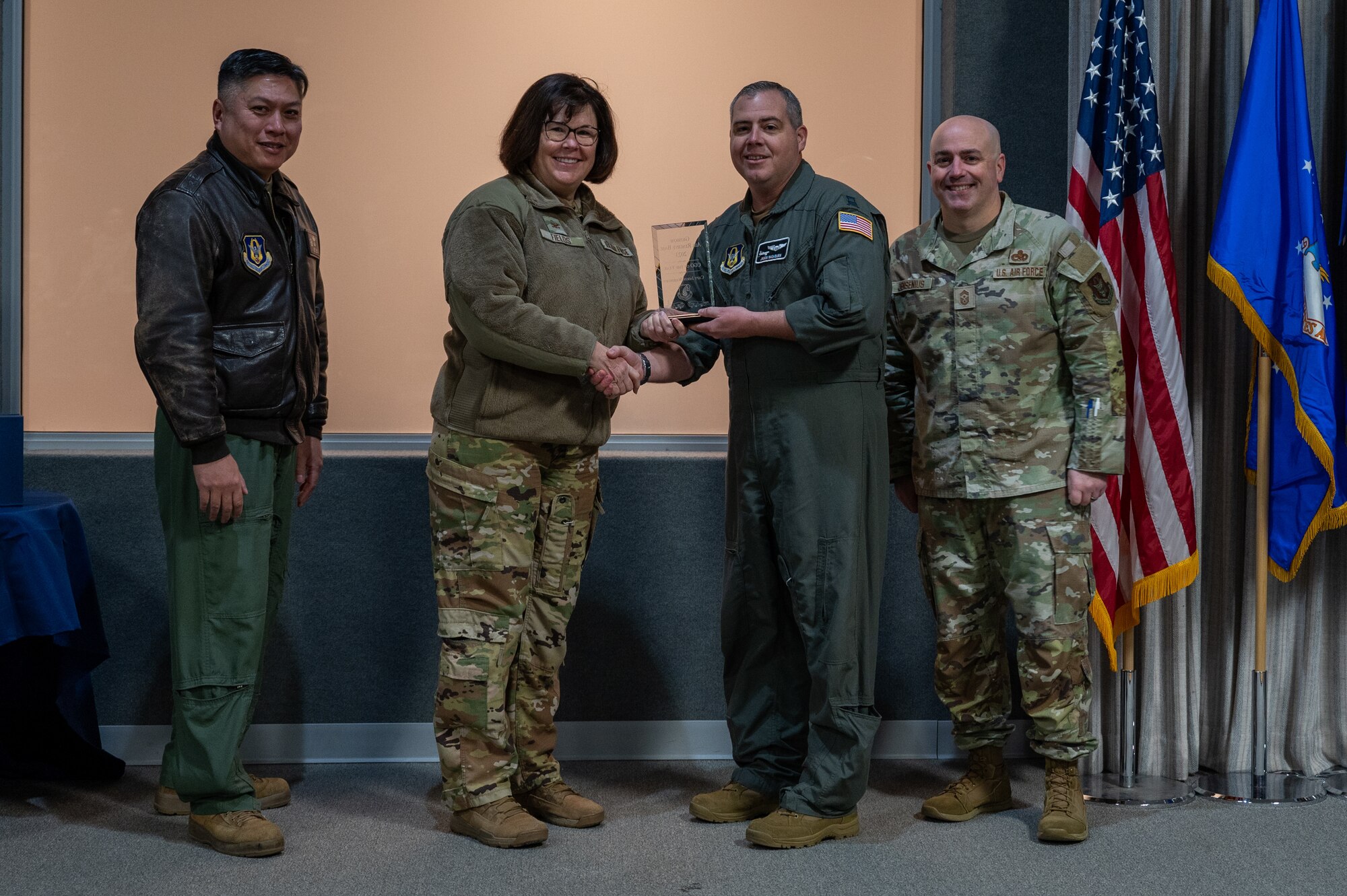 A man, with an award in his hand, shakes the hand of a woman. Two men, on either side of them, pose for a photo with the award. All are dressed in various U.S. Air Force uniforms.