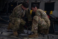 Two Airmen tie down cargo on a plane.
